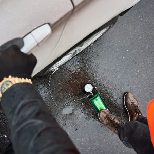 Close up of emergency auto mechanic legs inflating flat tire with air compressor. Man using air compressor to inflate tire while standing by the car on rainy road. Concept of emergency road service.